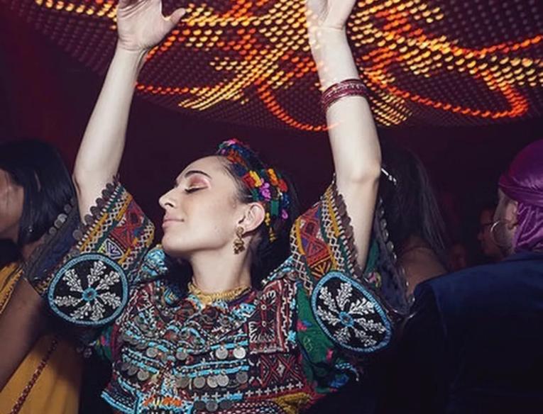 A dancer wearing an embroidered top with their hands in the air