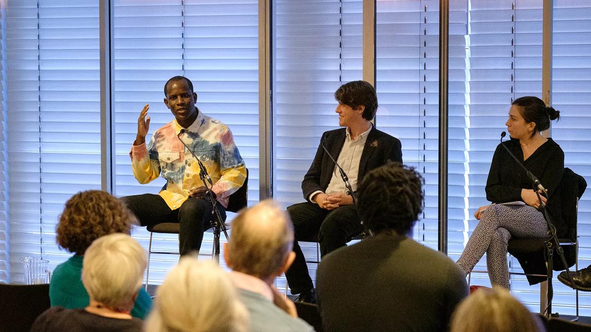 Three people, including musician Love Ssega, sitting on a podium in the Level 5 Function Room, speaking at a previous Philharmonia Insights Day