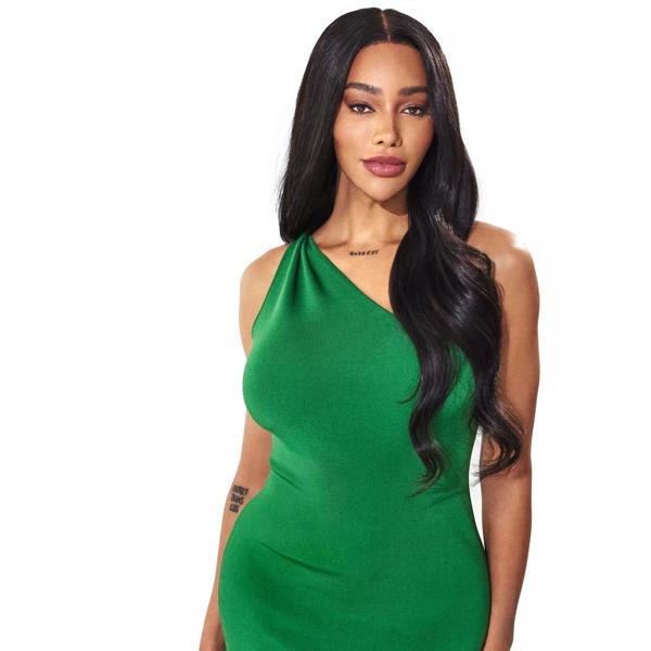 Munroe strikes a pose looking directly into camera wearing an emerald green one-shouldered dress. She has long dark hair that falls over her shoulder. 