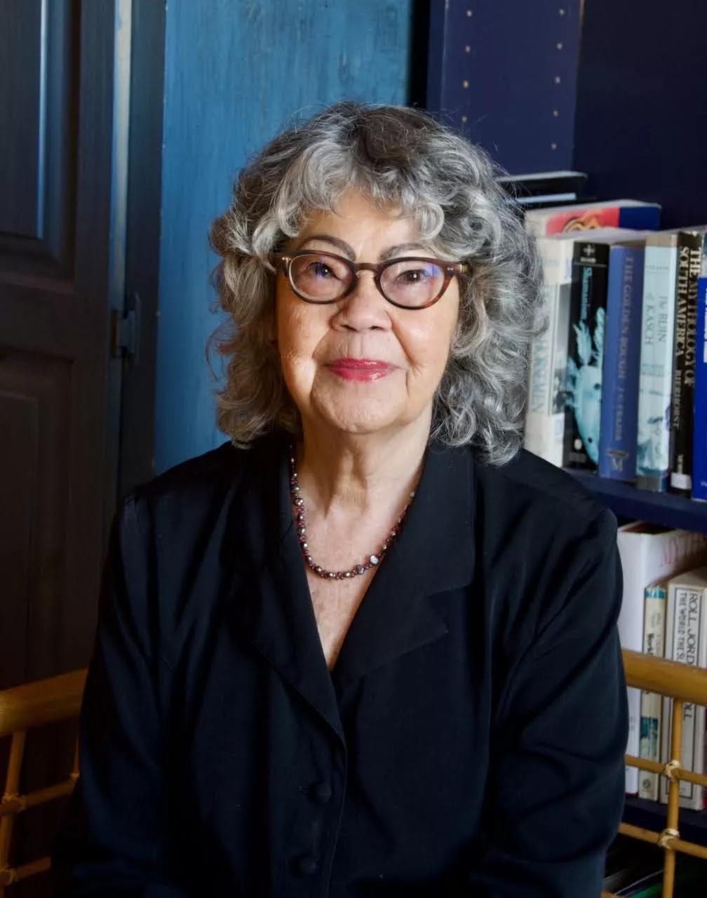 Poet Olive Senior sits in front of a bookshelf wearing glasses and a black top