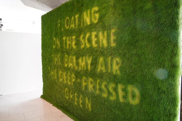 The words 'Floating on the scene the balmy air, the deep-pressed green' on wall made of grass