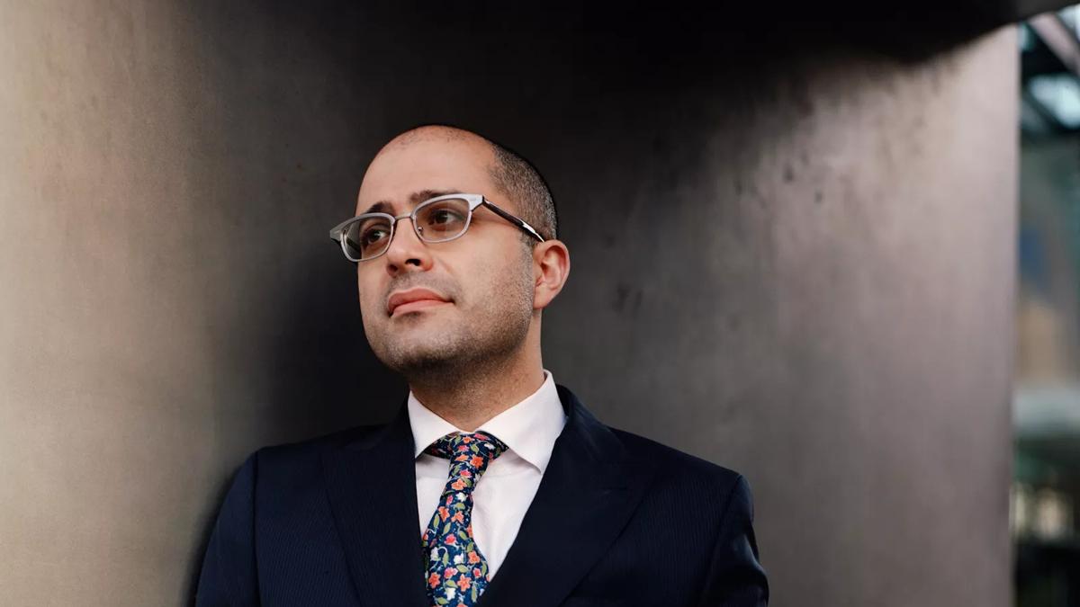 harpsichordist Mahan Esfahani in a suit leaning against a wall