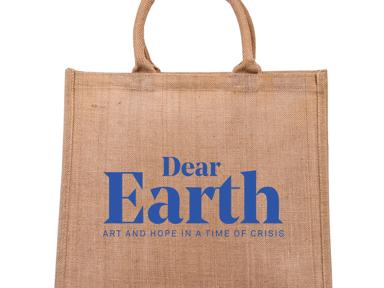 A brown hessian tote bag with 'Dear Earth: Art and Hope in a Time of Crisis' in blue letters