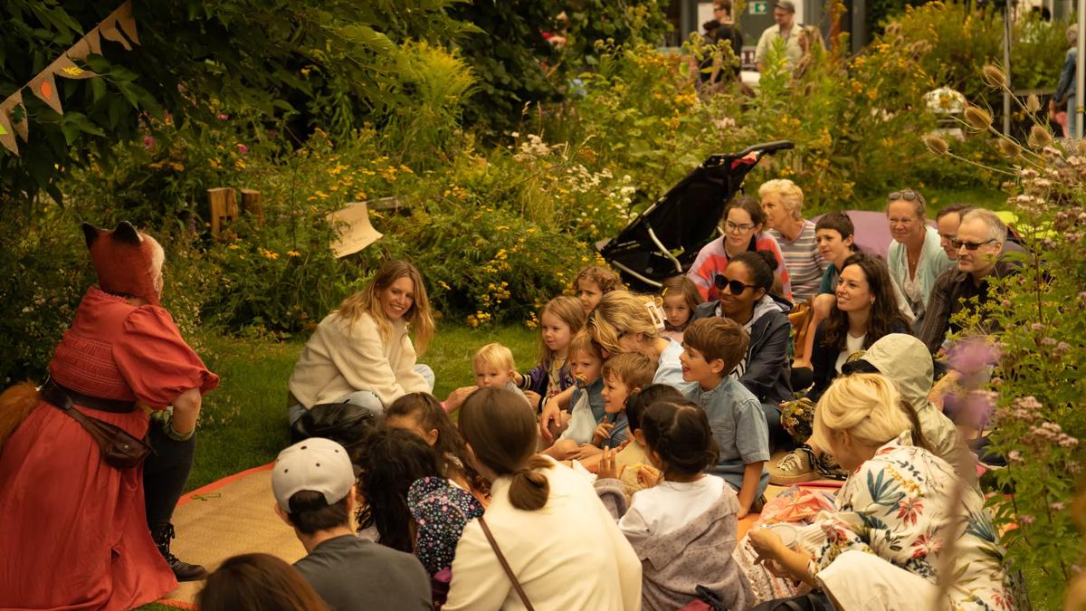 A group of children sat listening to performers in the Queen Elizabeth Roof Garden