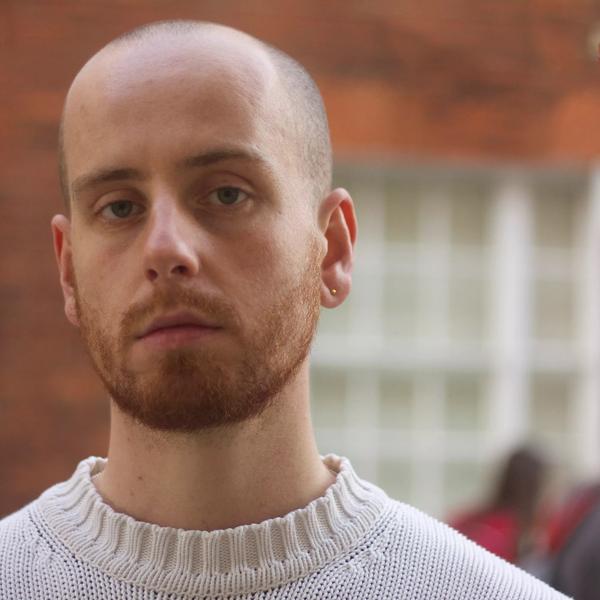 The poet Joe Carrick-Varty, a young White man with shaved head and stubble, wearing a cream-coloured jumper