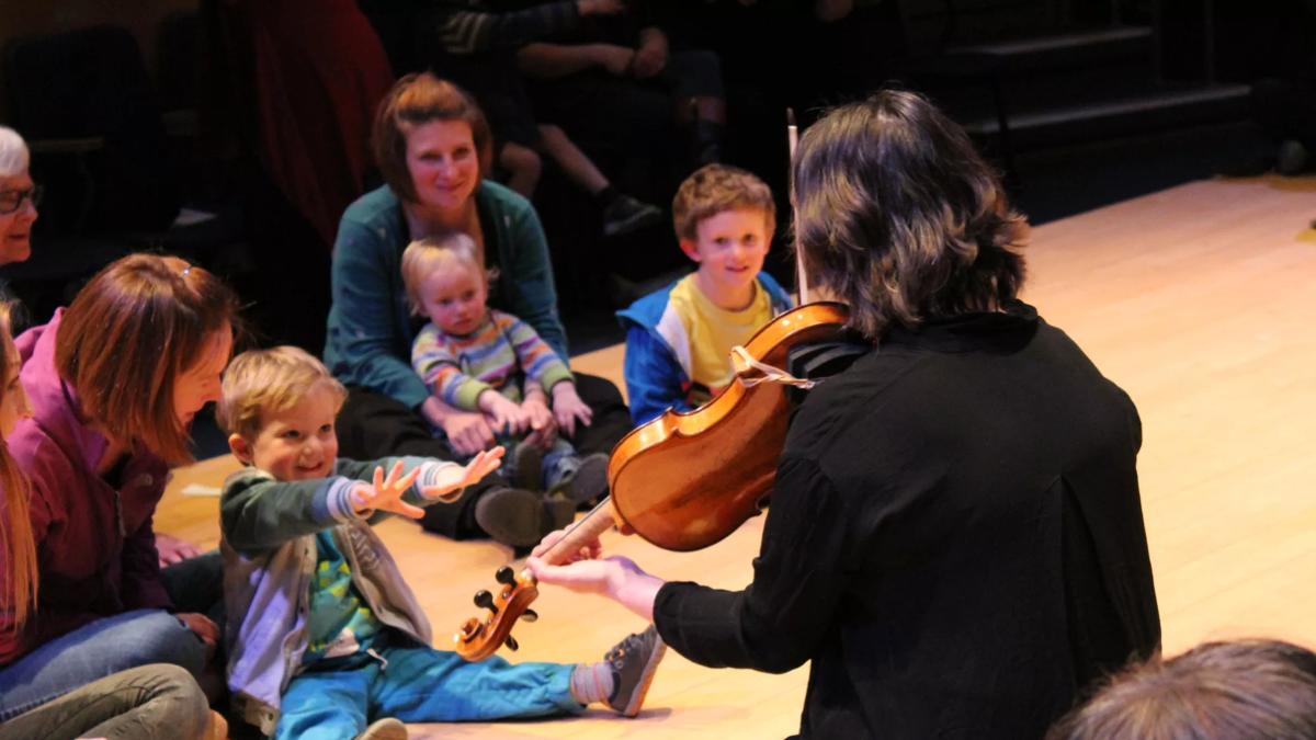 A woman playing the violin in front of toddlers and their carers