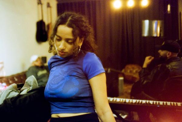 Lea Sen with dark curly hair wearing a blue top in a music studio