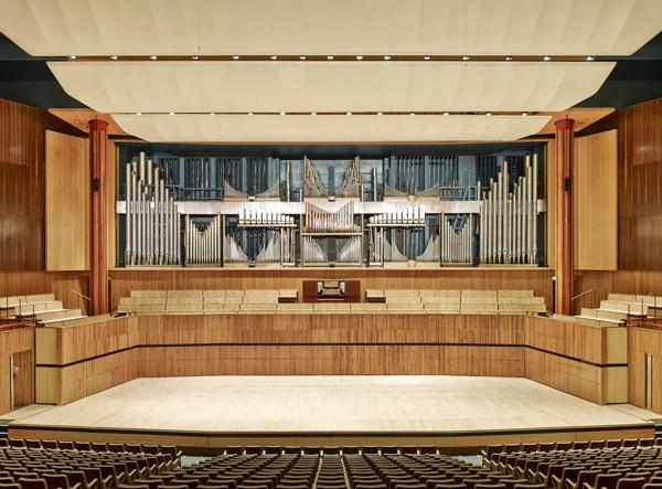 A front on wide view of the Royal Festival Hall organ with pipes on show, above the Royal Festival Hall stage, the front rows of seats are also just visible