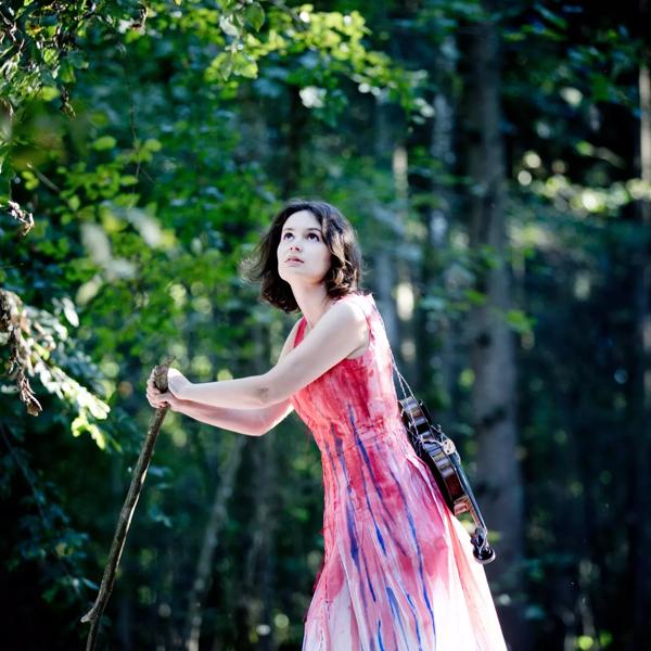 Patricia Kopatchinskaja with a violin on her back in a forest