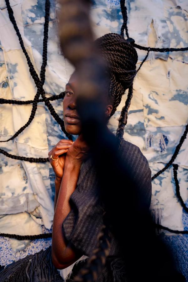 A black woman sits side on to the camera, her face is obscured by rope