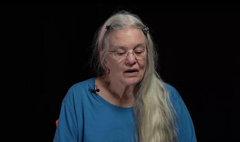 Sharon Olds, and older White woman with long white hair hanging over her left shoulder reads from their TS Eliot Prize shortlisted collection against a black background