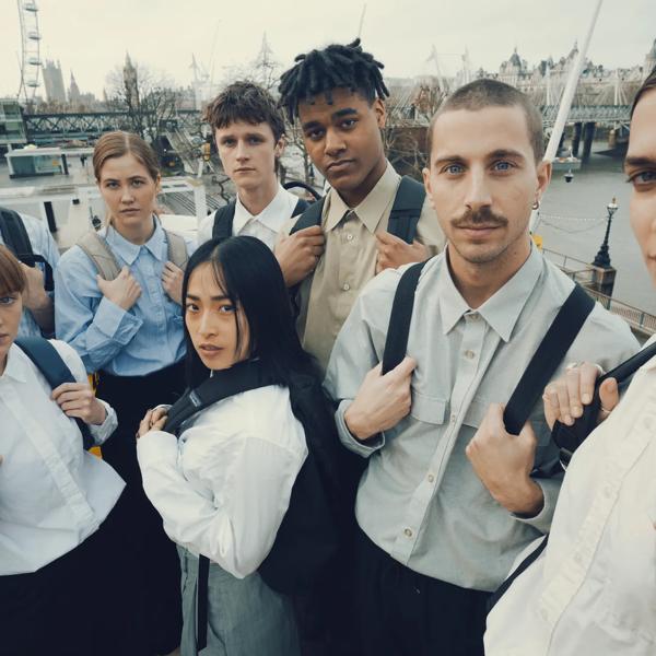 eight people stand on a staircase overlooking the southbank centre, they're all wearing white shirts and holding black backpack straps across their chests.