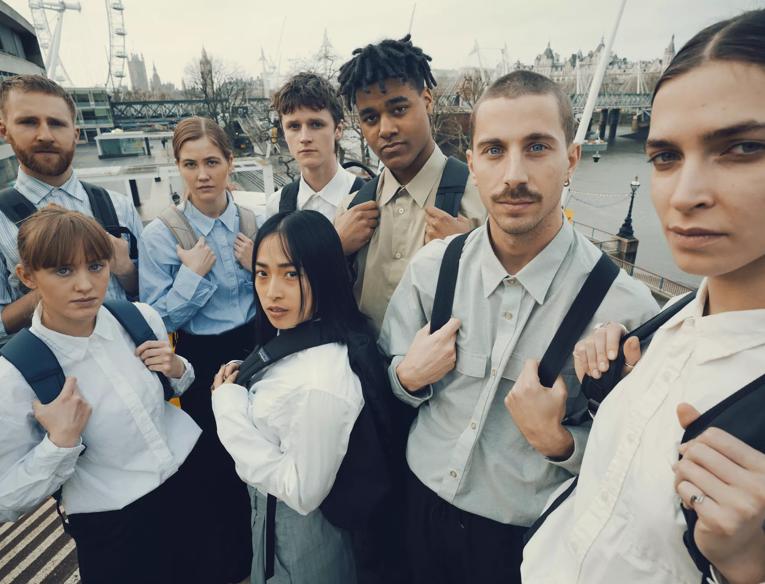eight people stand on a staircase overlooking the southbank centre, they're all wearing white shirts and holding black backpack straps across their chests.