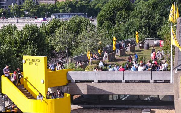 The Southbank Centre's Queen Elizabeth Hall Roof Garden in the summer with people sat around chatting, as seen from the Level 5 balcony of the Royal Festival Hall