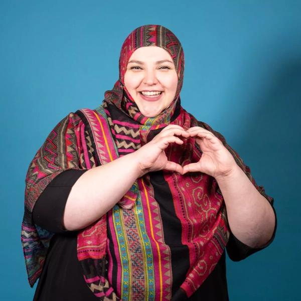 A woman dressed in a colourful hijab makes a shape of a heart with her hands