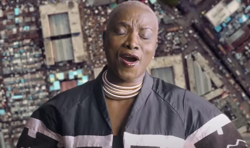 Angelique Kidjo sings in front of an overhead image of an African city
