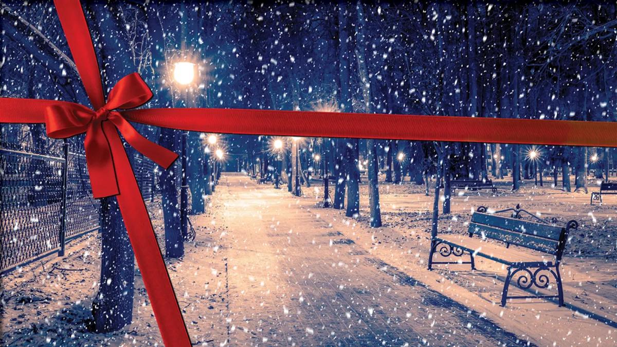 Shows a snowscape of a throughway in a park at night. There is a graphic of a red ribbon tied around it so it looks like a present.