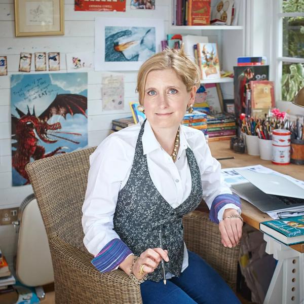 Author Cressida Cowell sits with a pencil in her hand in front of her "How to Train Your Dragon" illustrations. 