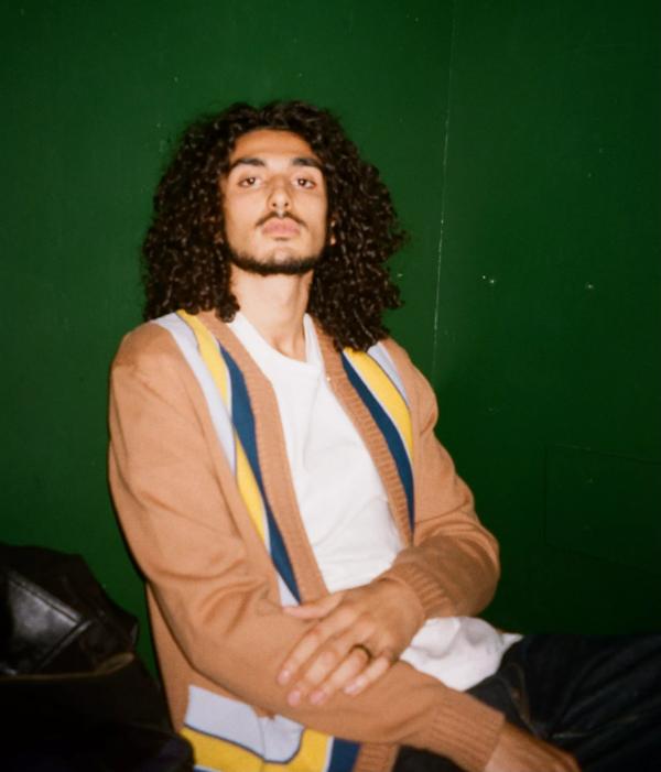 A man with curly hair wearing an orange and white jumper with stripes