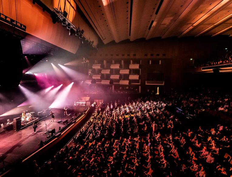 A band on stage performing in front of a full crowd in the Royal Festival Hall