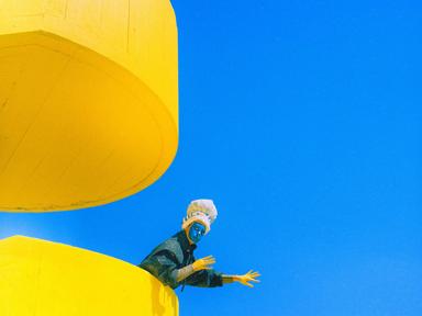 Artistic shot of a blue painted face person leaning over a yellow staircase over the blue sky