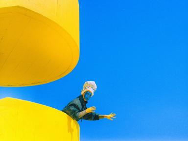 Artistic shot of a blue painted face person leaning over a yellow staircase over the blue sky