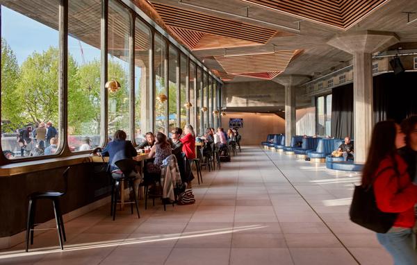 Queen Elizabeth Foyer, showing brutalist architecture, people sitting at high stools chatting with riverside views.