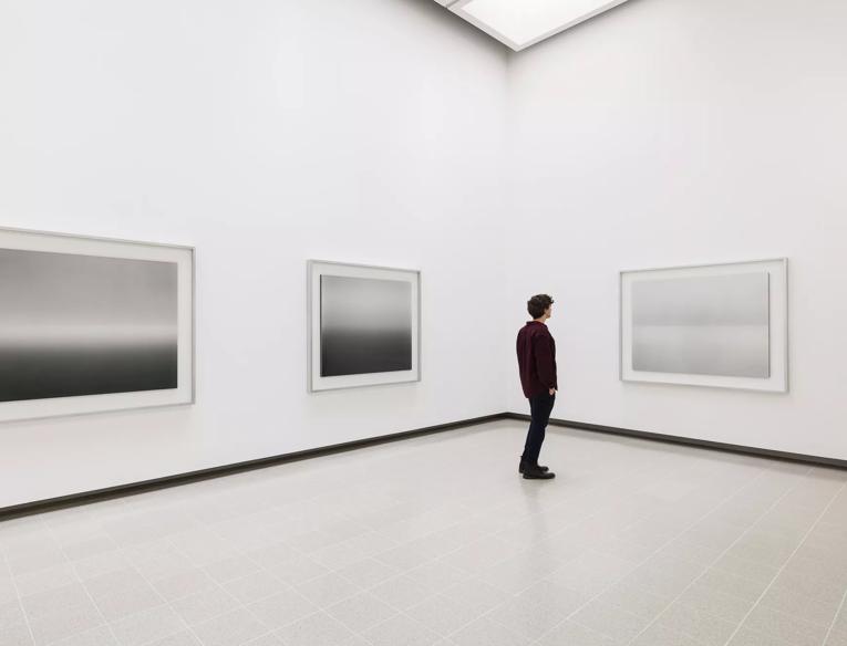 A person stands in front of three of Hiroshi Sugimoto's black and white Seascapes photographs.