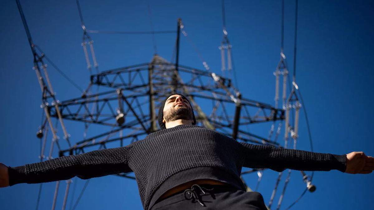 Looking up at multi instrumentalist Manu Delago under an electricity pylon
