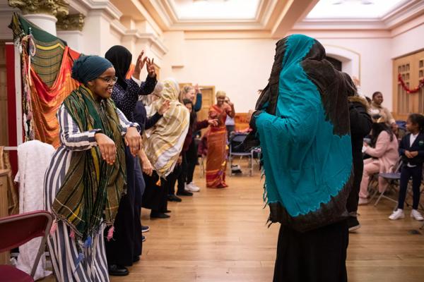 Somali Folk Dance - 1 smiling teacher gesturing with participant mimicking action in response. Other participants in the background