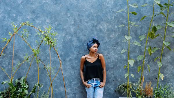 A woman wearing jeans and a black strappy top next to plants