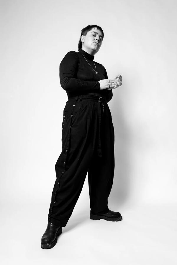 Black and white portrait of Amor Ante standing and looking down at the camera. 