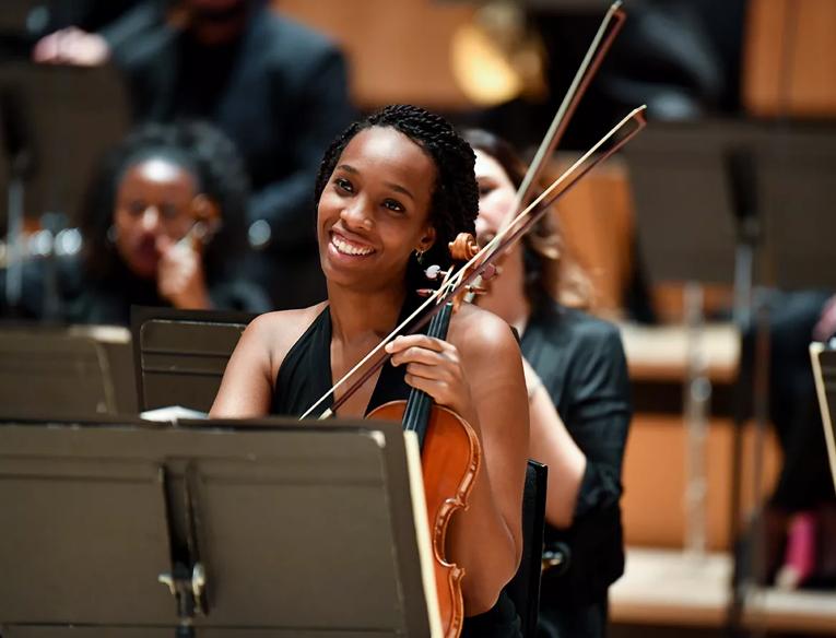 A violinist smiling at the Chineke! Orchestra: Symphonic Celebration