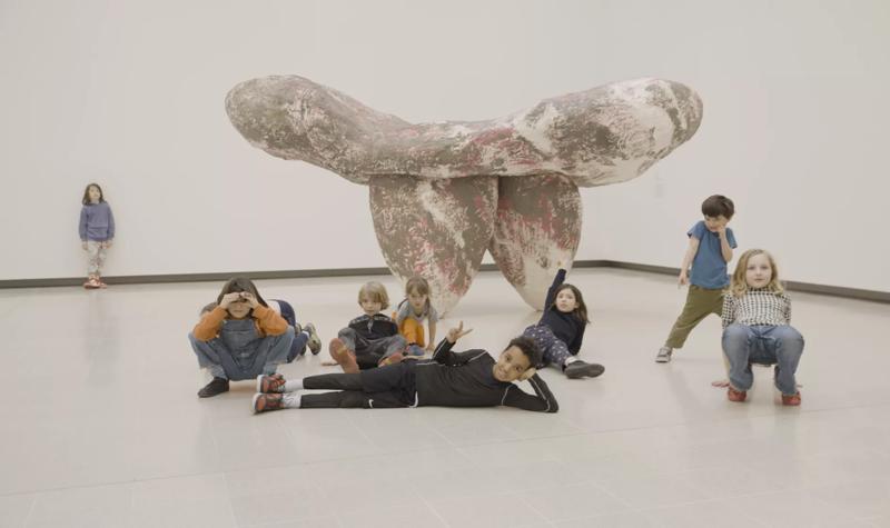 Several young children sit around a sculpture, part of the When Forms Come Alive exhibition, in the white space of the Hayward Gallery