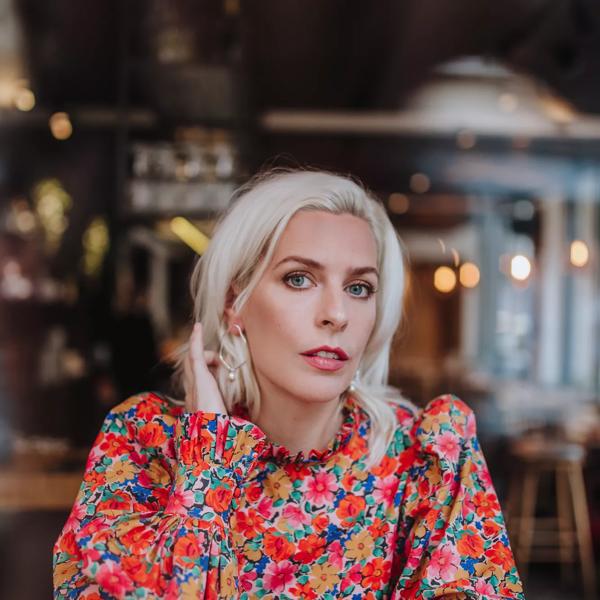 Sara Pascoe sits at a table wearing a floral top