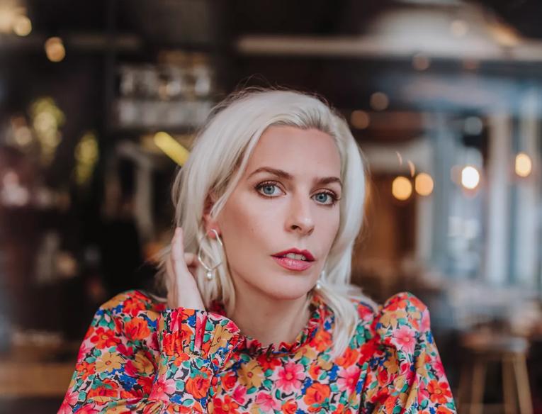 Sara Pascoe sits at a table wearing a floral top