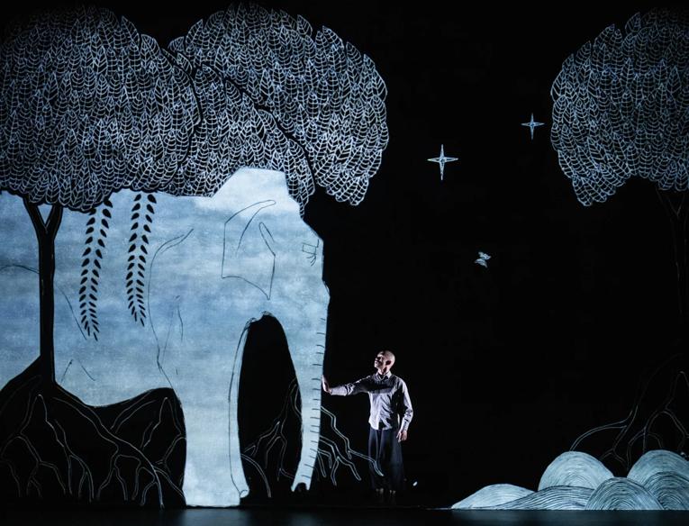 Animated image of an elephant in a forest with a non-animated male reaching out to the elephant.