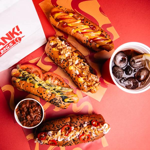Photo from above of 4 hot dogs, a coke and chilli on a red background