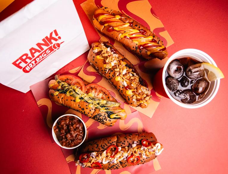 Photo from above of 4 hot dogs, a coke and chilli on a red background