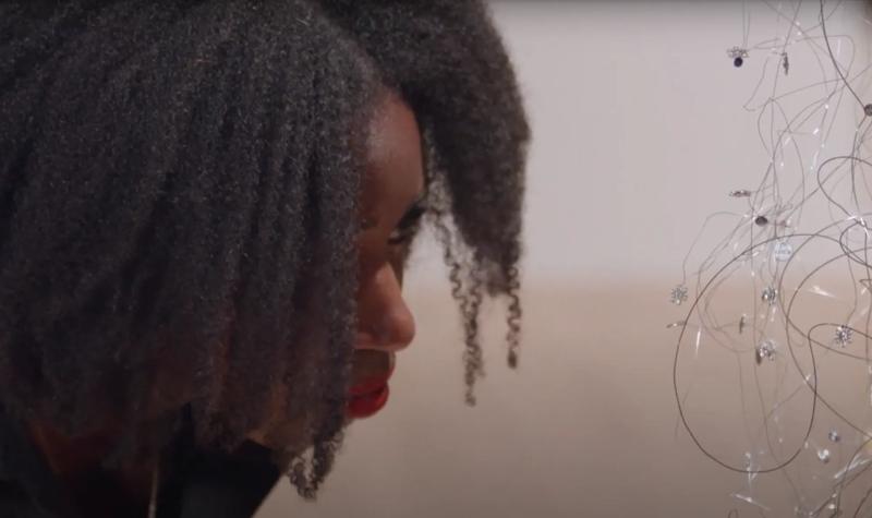 The poet Victoria Adukwei Bulley examining a piece of work within Igshaan Adams: Kicking Dust at Hayward Gallery