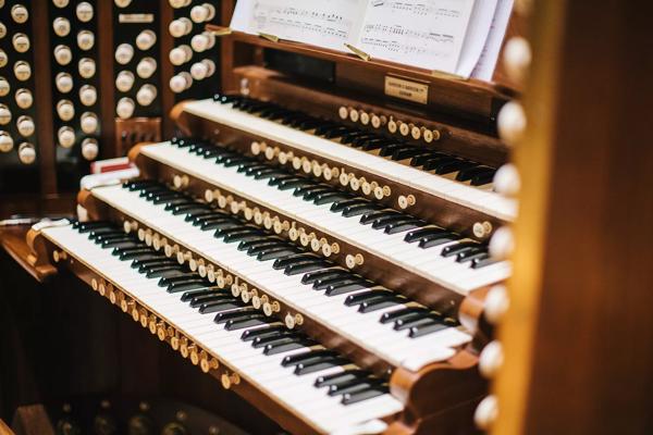 A close up of the keys of the Royal Festival Hall organ, showing four keyboards on top of each other, with some of the round white stops visible on either side. The bottom of an open music score is also visible above the keys