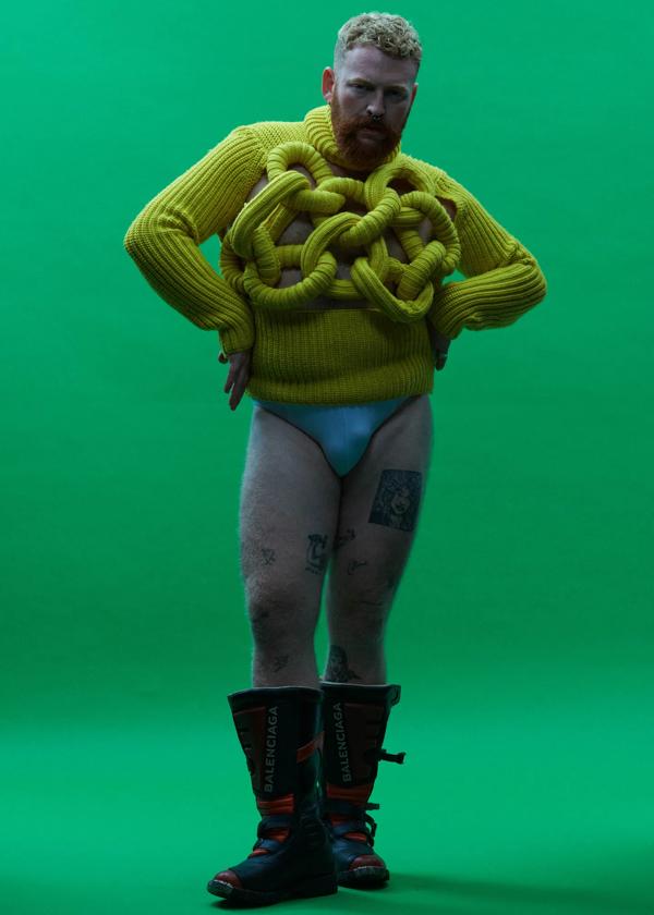 Musican Tom Rasmussen stands in pants and a lime green jumper in front of a bright green background.