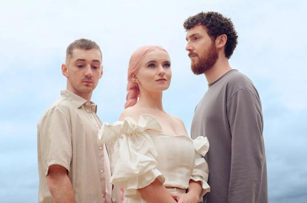 Three members of Clean Bandit standing in front of a blue background