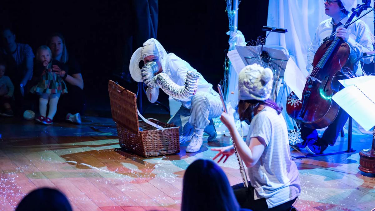 Musicians and a performer in an elephant costume are performing amongst a winter wonderland set. 