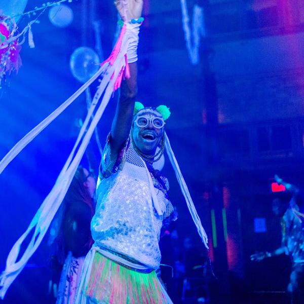 Performer on stage holding their hand up and cheering in a blue light
