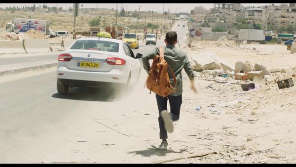 A man runs down a sandy road with an orange backpack on. 