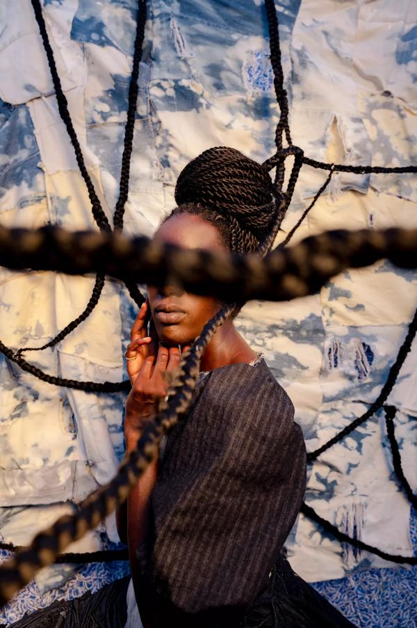 A black woman sits side on to the camera, her face is obscured by rope