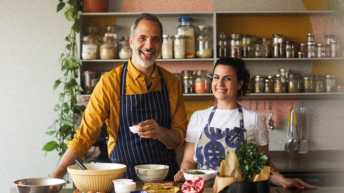 Yotam Ottolenghi on the left holding bowl & Noor Murad on the right. Seen on their cookery set with apron