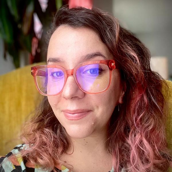 Julia Sanches, a Brazilian woman with pink hair and red-framed glasses