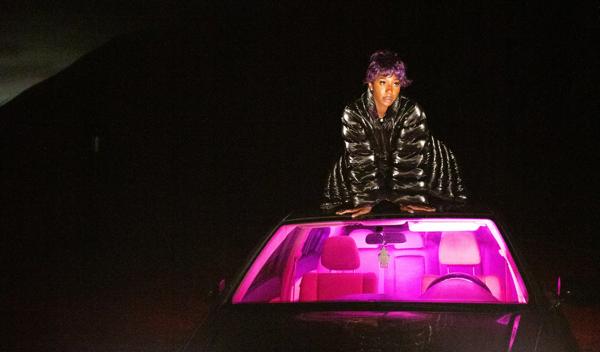 A woman with purple hair posing on top of a car